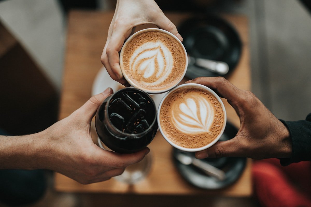 Drie warme koffies samen geheven boven een houten tafeltje